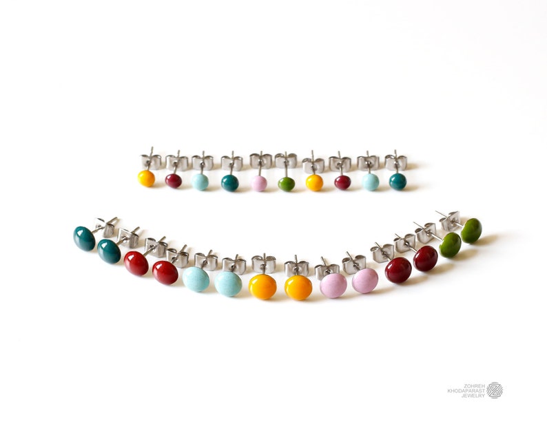 May include: A set of 18 colorful enamel stud earrings. The earrings are arranged in a semi-circle pattern on a white background. The colors include red, orange, yellow, green, blue, and purple.