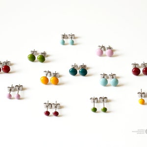 May include: Assortment of colorful enamel stud earrings in various colors including red, green, blue, yellow, and pink. The earrings are displayed on a white surface.