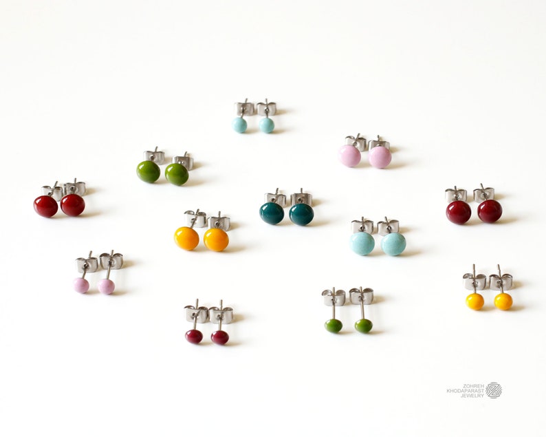 May include: Assortment of colorful enamel stud earrings in various colors including red, green, blue, yellow, and pink. The earrings are displayed on a white surface.