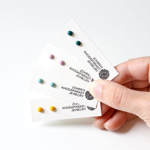 May include: Four cards with pairs of small, round, colorful earrings. The cards have the text "Zohreh Khodaparast Jewelry" printed on them.