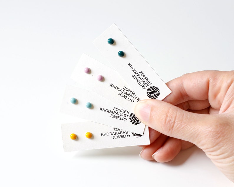 May include: Four cards with pairs of small, round, colorful earrings. The cards have the text "Zohreh Khodaparast Jewelry" printed on them.