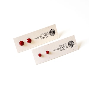 Könnte beinhalten: Zwei Karten mit roten runden Ohrsteckern darauf. Die Karten tragen den Text "Zohreh Khodaparast Jewelry".