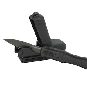 Può includere: Un coltello tattico nero con un fodero nero. Il coltello ha un'impugnatura nera con una presa testurizzata e una lama nera con un bordo argentato. Il fodero ha una cinghia nera e una fibbia nera.