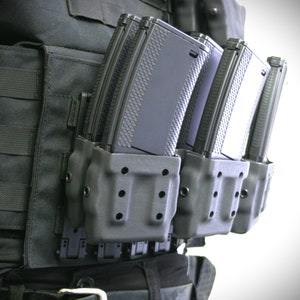 Może przedstawiać: Czarna taktyczna kamizelka z wieloma kieszeniami na magazynki przymocowanymi do przodu. Kieszenie wykonane są z czarnego plastiku i mają fakturowaną powierzchnię. Kieszenie są zaprojektowane do przechowywania wielu magazynków.