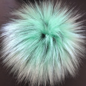 May include: A fluffy green and black faux fur pom pom. The pom pom is round and has a soft, plush texture.