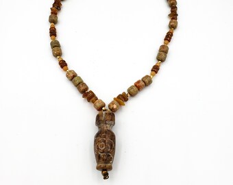 May include: A brown and beige stone necklace with a carved stone pendant. The pendant is shaped like a vase with a floral design.