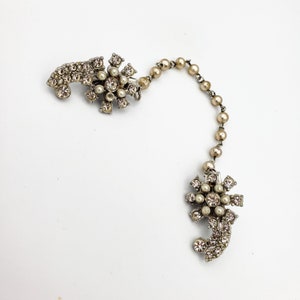 May include: A silver chain with two decorative floral brooches, each with a cluster of clear rhinestones and faux pearls.