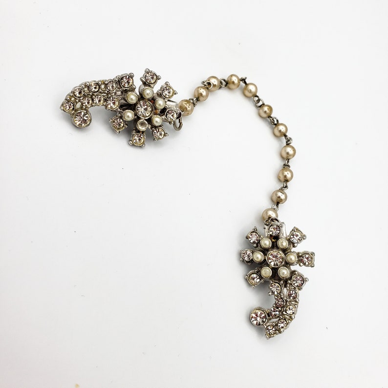 May include: A silver chain with two decorative floral brooches, each with a cluster of clear rhinestones and faux pearls.