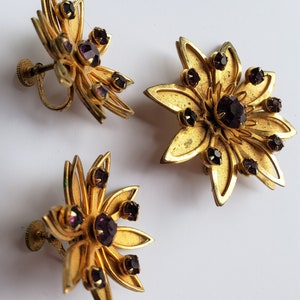 May include: A pair of gold tone earrings with purple rhinestones in a flower shape.