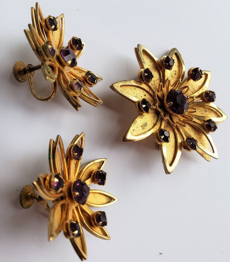 May include: A pair of gold tone earrings with purple rhinestones in a flower shape.