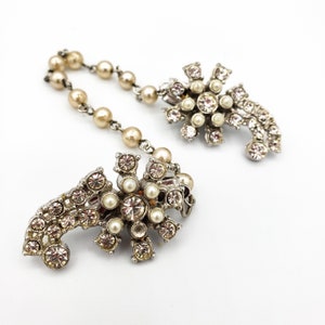 May include: A pair of vintage silver tone brooch clips with a pearl and rhinestone design. The clips are connected by a chain of faux pearls.