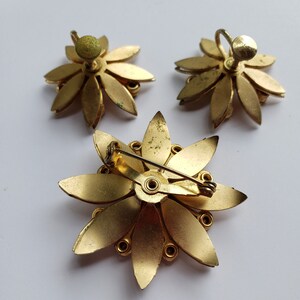 May include: A set of three gold-toned flower-shaped brooches. Two of the brooches are earrings with a post and back closure. The third brooch has a pin and clasp closure.