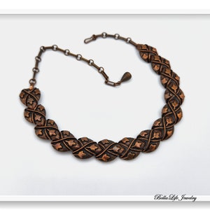 May include: A copper necklace featuring a chain and a series of interlocking oval links, each with a decorative pattern of small leaves.
