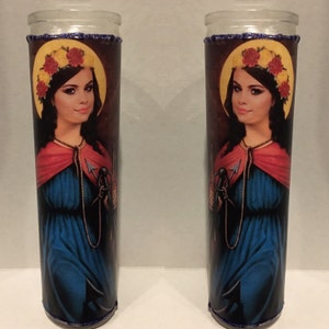 May include: Two glass candle holders with a printed image of a woman with a crown of flowers, wearing a blue dress and red robe, holding an anchor and a rope. The background is brown.