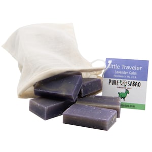 May include: A set of six small lavender-colored soap bars in a white muslin bag. The soap bars are labeled "Little Traveler Lavender Calm Handmade in the U.S.A. PURE SABAO HANDCRAFTED SOAPS  asabao.com"