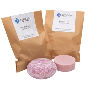 May include: Two brown paper bags with labels that read "REDEEM SOAP COMPANY Lavender Calm Shampoo Bar" and "REDEEM SOAP COMPANY Lavender Calm Conditioner Bar". The bags contain two solid purple shampoo and conditioner bars.
