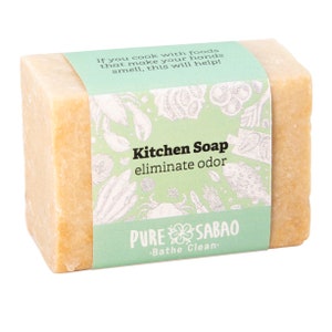 Könnte beinhalten: Eine hellbraune Küchenseife mit einem grünen Etikett, auf dem "Kitchen Soap eliminate odor" und "PURE SABAO .Bathe Clean." steht.
