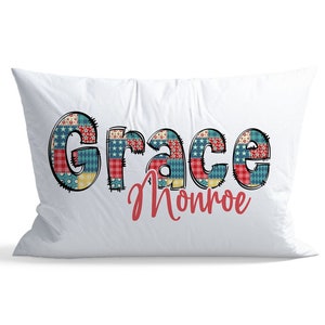 May include: White pillow with the name "Grace Monroe" printed in red and black. The letters are made up of a patchwork pattern of red, white, blue, and yellow.