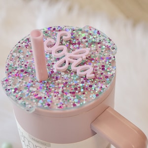 May include: Pink tumbler with a clear lid and a pink straw. The lid has a pink glitter design and the name "Sofia" written on it.