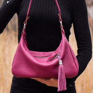 May include: A pink leather handbag with a silver zipper and a tassel. The bag has a shoulder strap and is made of a textured leather.
