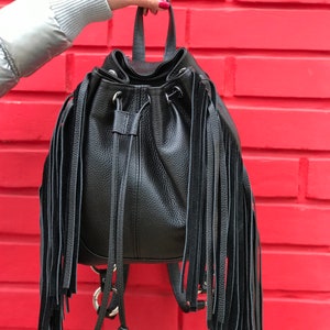 May include: Black leather backpack with long fringe details. The backpack has a drawstring closure and adjustable straps.
