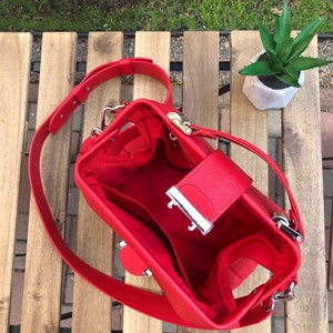 May include: A red leather handbag with a silver clasp and a long strap. The bag is open and the inside is lined with red fabric.