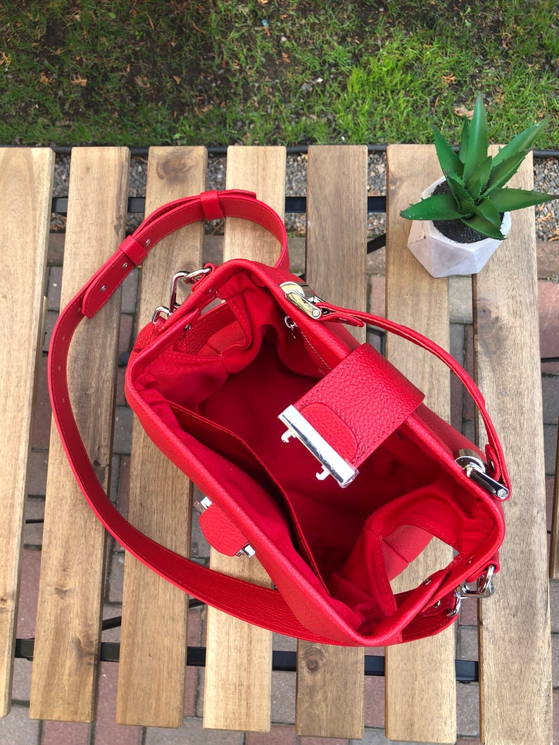 May include: A red leather handbag with a silver clasp and a long strap. The bag is open and the inside is lined with red fabric.