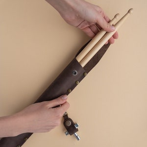 May include: A brown leather drumstick holder with a metal snap closure and a key chain attached. The holder is open and two wooden drumsticks are inside.