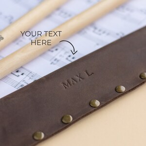 May include: Brown leather drumstick holder with brass rivets and the name "MAX L." embossed on the front.