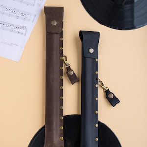 May include: Two leather cases for musical instruments, one brown and one black, with gold-colored rivets and a strap. The cases are on top of black vinyl records.