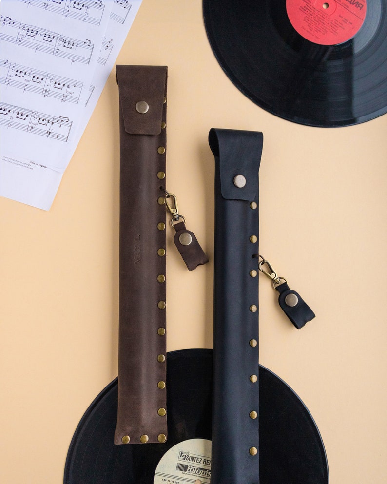 May include: Two leather cases for musical instruments, one brown and one black, with gold-colored rivets and a strap. The cases are on top of black vinyl records.