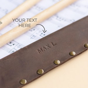 May include: A brown leather drumstick holder with brass rivets and the name "MAX L." embossed on the front.