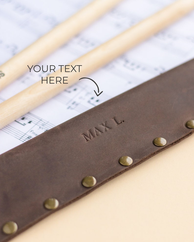 May include: A brown leather drumstick holder with brass rivets and the name "MAX L." embossed on the front.