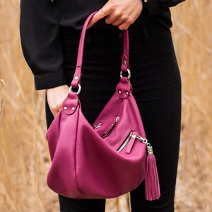 May include: A deep pink leather handbag with a long strap and a tassel zipper pull.