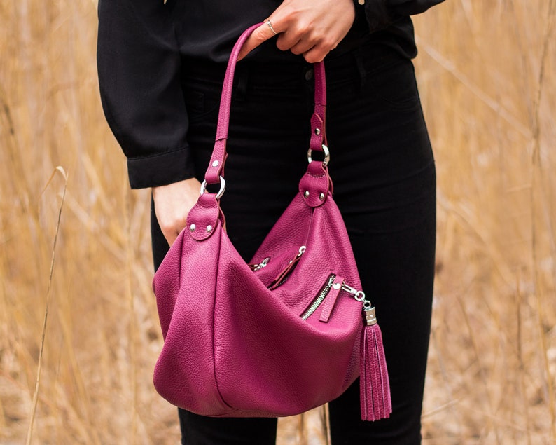 May include: A deep pink leather handbag with a long strap and a tassel zipper pull.