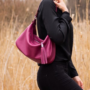 May include: A deep pink leather handbag with a silver tassel and a zipper closure. The bag is worn over the shoulder.