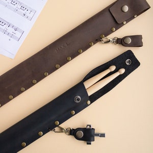 May include: Two leather cases for drumsticks. The brown case has the name "MAX L." embossed on it. Both cases have a metal clasp and a leather strap.