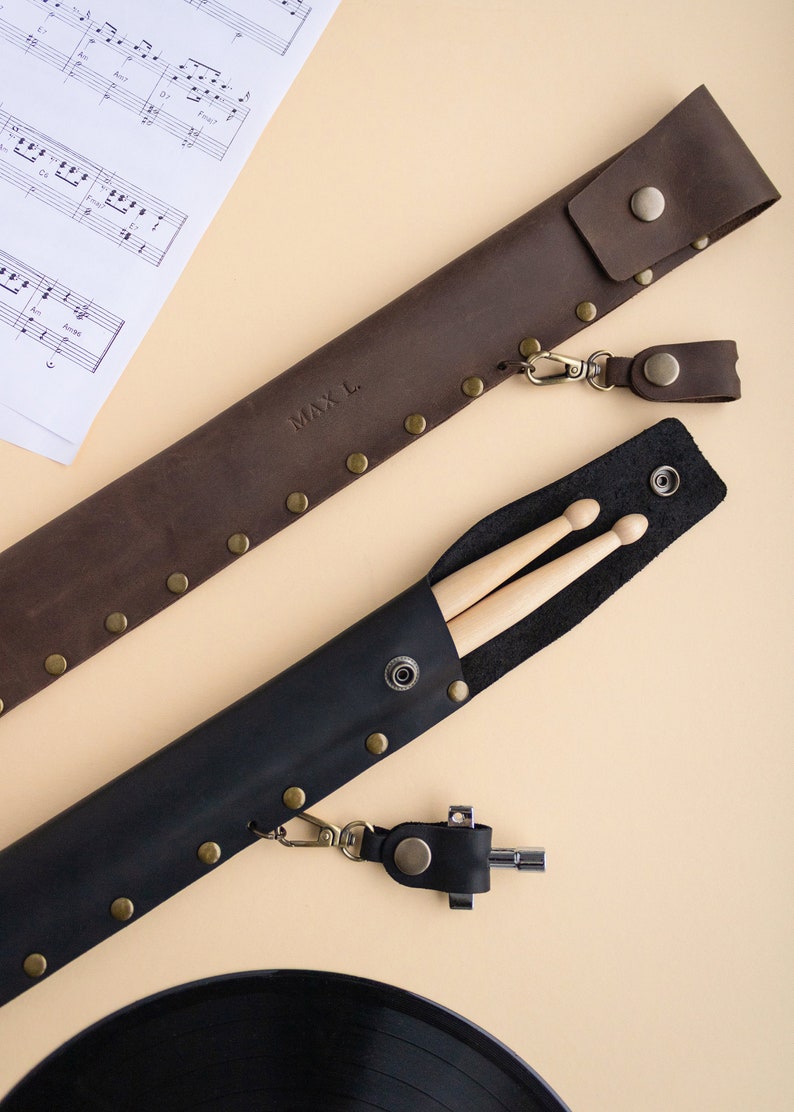 May include: Two leather cases for drumsticks. The brown case has the name "MAX L." embossed on it. Both cases have a metal clasp and a leather strap.