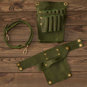 K&ouml;nnte beinhalten: Gr&uuml;ner Leder-Werkzeugg&uuml;rtel mit abnehmbarem Riemen und mehreren Taschen zum Verstauen von Werkzeugen. Der G&uuml;rtel hat eine Messing-Schnalle und Nieten.
