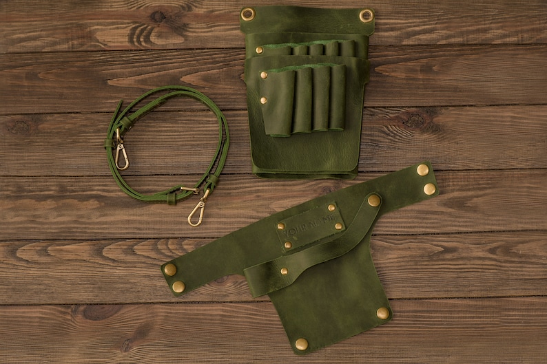 K&ouml;nnte beinhalten: Gr&uuml;ner Leder-Werkzeugg&uuml;rtel mit abnehmbarem Riemen und mehreren Taschen zum Verstauen von Werkzeugen. Der G&uuml;rtel hat eine Messing-Schnalle und Nieten.