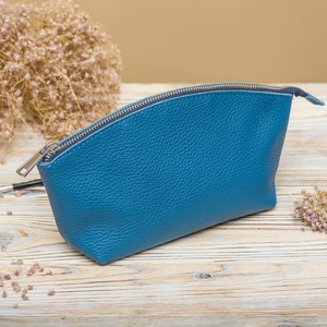 May include: A blue leather zippered pouch or cosmetic bag. The bag is on a light wood surface.