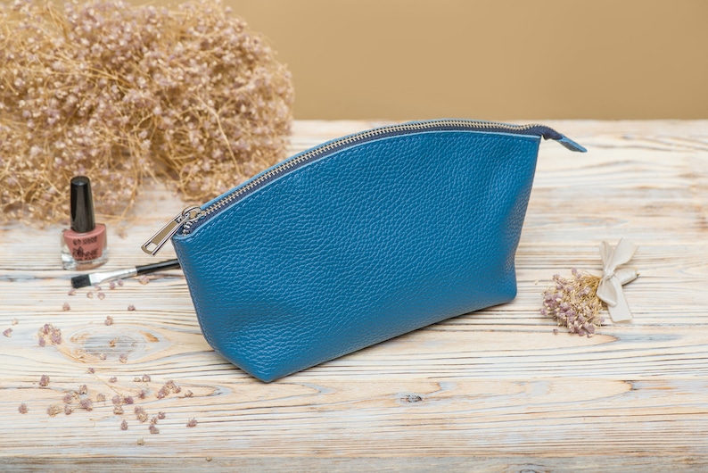 May include: A blue leather zippered pouch or cosmetic bag. The bag is on a light wood surface.