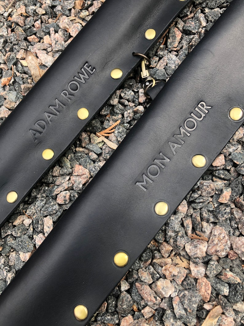 May include: Two black leather straps with gold metal rivets and the text "ADAM ROWE" and "MON AMOUR" embossed on them.