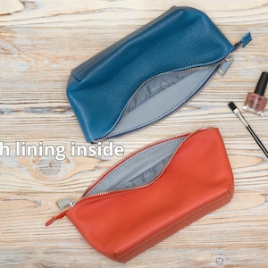 May include: Two zippered pouches, one blue and one orange, with a gray lining. The pouches are open and the lining is visible. The pouches are on a wooden surface.