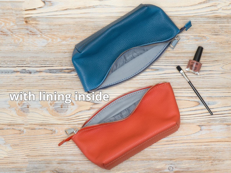 May include: Two zippered pouches, one blue and one orange, with a gray lining. The pouches are open and the lining is visible. The pouches are on a wooden surface.