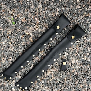 May include: Two black leather sheaths with gold studs and the text "ADAM NOIR" and "ROMAN NOIR" on them.