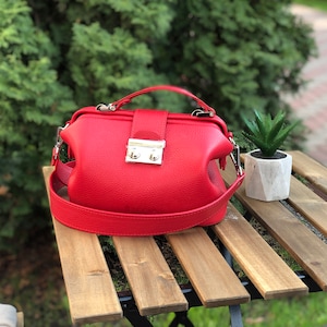 May include: A red leather doctor bag style handbag with a silver clasp and a long strap.