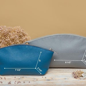 May include: Two leather cosmetic bags, one blue and one gray, with measurements in inches. The bags are on a wooden surface.