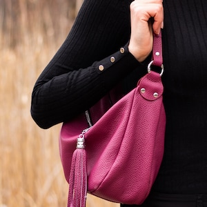 May include: A deep pink leather shoulder bag with a silver zipper and a tassel. The bag has a long strap and is worn over the shoulder.