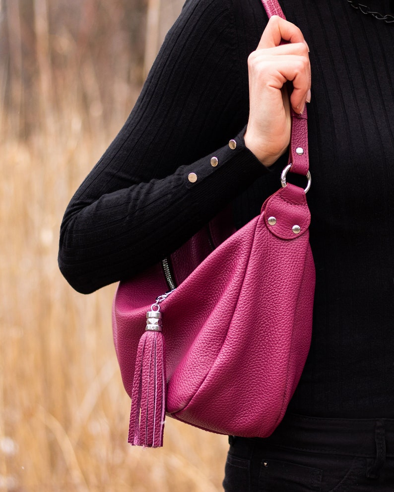 May include: A deep pink leather shoulder bag with a silver zipper and a tassel. The bag has a long strap and is worn over the shoulder.
